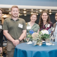 5 GVSU Alumni smile at camera with a table in front